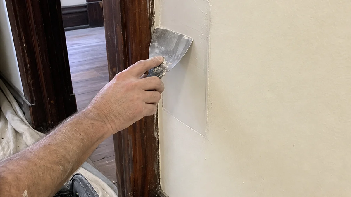 Handyman finishing plaster patch beside original wood trim Scranton Pennsylvania Lackawanna County coal-era home repair